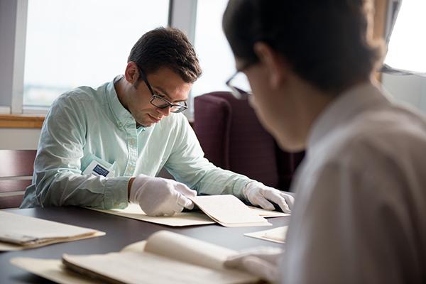 Two students looking over historical documents using gloves.